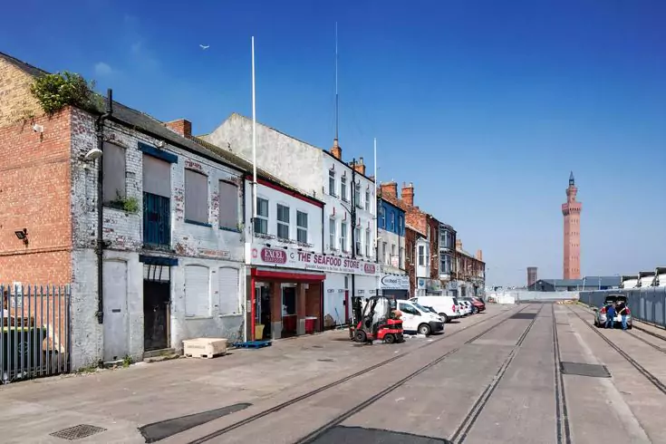 Street view of Grimsby, featuring old buildings, a seafood store, and the Grimsby Dock Tower in the background.