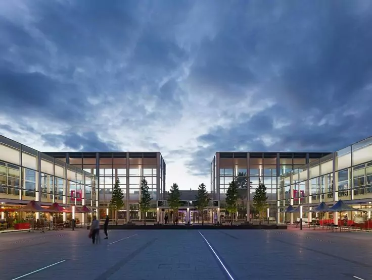 A modern architectural view of Milton Keynes, England, at dusk, featuring illuminated pathways and contemporary buildings.